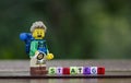 Lego hiker holding compass with word strategy using colorful alphabet beads.