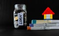 A lego home toy on top of three money bundles and defocused glass jar with coins and LOAN label behind