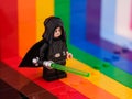 A Lego Luke Skywalker minifigure with a lightsaber standing against a rainbow backdrop