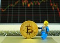 A LEGO man carrying a gold bitcoin on a notebook computer with stock graph in the background