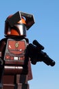 Lego Mandalorian figure in brown and orange coloured armor and helmet, with blaster rifle in left hand
