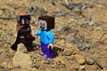 LEGO Mandalorian greets LEGO Minecraft Steve figure on arid desert like soil, summer daylight sunshine.