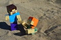 LEGO Minecraft action figure of Steve pulling his female friend Alex from shifty sand pit on a beach. Summer afternoon sunshine.