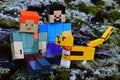 LEGO Minecraft action figures of Alex and Steve sitting on frozen winter moss with ocelot cat in front.