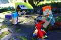 LEGO Minecraft action figures of Steve and Alex doing push-ups exercise on real world moss covered wood, red parrot is watching.