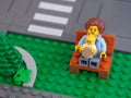 A Lego mother minifigure with a child in a baby carrier sitting on a bench in a city park