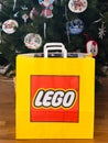 A Lego paper bag with a Lego set in it near a Christmas tree decorating with handmade Christmas ornaments