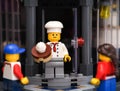 A Lego pastry chef minifigure with a cake standing on the doorstep of a his bakery and two children looking to him