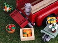 A Lego Pickup Truck with milk bucket in its bed, some crates of vegetables and a wheelbarrow with flowers on a grass background