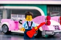 Lego pink 1950s-style convertible and rock-n-roll star minifigure with guitar near in city street