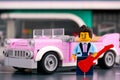 Lego rock-n-roll star minifigure with guitar near pink 1950s-style convertible