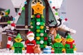 Lego Santa Claus, Elves and Reindeer standing near Christmas tree opposite Elf Club House