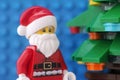 A Lego Santa Claus minifigure standing next to a Christmas tree against a blue baseplate background