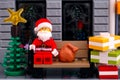 Lego Santa Claus sitting on the bench outdoors with stack of gifts and Christmas tree