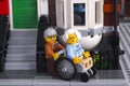 Lego senior couple near his house in the street. Woman sit in wheelchair, man help her