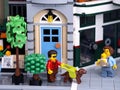 A Lego visually impaired man minifigure with a guide dog walking on a city street with a Lego mother with a baby walking towards