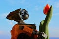 LEGO Wall-E robot figure from Pixar animated movie holding spring orange to yellow tulip flower, blue skies in background