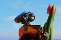 LEGO Wall-E robot figure from Pixar animated movie holding spring orange to yellow tulip flower, blue skies in background