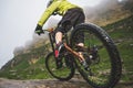 Legs of bicyclist and rear wheel close-up view of back mtb bike in mountains against background of rocks in foggy Royalty Free Stock Photo