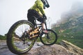 Legs of bicyclist and rear wheel close-up view of back mtb bike in mountains against background of rocks in foggy Royalty Free Stock Photo