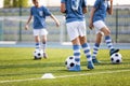 Legs of Boys Soccer Players on Grass Training Venue. Kids in Light Blue Shirts Kicking Soccer Balls