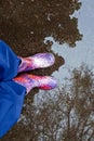 Legs bright rubber boots stand in a puddle. Trees are reflected in calm water. Vertical photo