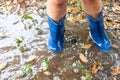 Legs of child wearing pair of blue rubber boots in water puddle