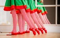 Legs of children dressed in costumes of Christmas elves practicing at a ballet bar in front of a mirror in a spacious white studio