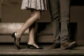 Legs of a couple standing and kissing on a wooden bench