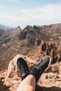Legs crossed in relaxed pose on top of a mountain. Girl`s legs wearing old and worn black and white sneakers