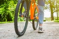 The legs of a cyclist and part of a bicycle on a dirt road in sunlight