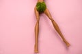 legs of a doll with a green leaf covering the crotch on a pastel pink background