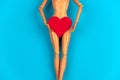 legs of a doll with a red heart covering the crotch on a vibrant blue background