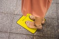 Legs and feet of a person waiting in line and standing inside yellow floor sign keep your distance with social