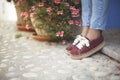 Legs of a female in jeans and elegant red sneakers white laces standing ner the flower pots Royalty Free Stock Photo