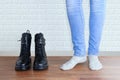 Legs of a girl in blue jeans and socks next to a pair of black boots.