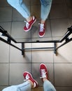 Legs of a girl in jeans and red sneakers in the reflection of the mirror.