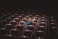 Legs of a girl in jeans are shown from behind the seats in the theater