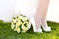 Legs of girl or bride in white shoes with bows and round wedding bouquet Royalty Free Stock Photo