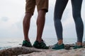 The legs of the guy and the girl standing on the kamnnisty beach, the guy and the girl sits on stones and drink from thermo mugs. Royalty Free Stock Photo