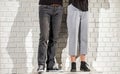Legs of a guy and a girl in trousers and shoes on a background of a white brick wall