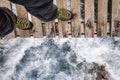 Legs in hiking shoes on the edge of a wooden bridge over stormy water Royalty Free Stock Photo