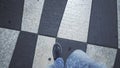 Legs of independent young man walking chessboard square, breaking rules, pov