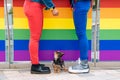 Legs of a lesbian couple iin front of a railing with the LGBTQ + flag with their dog