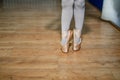 Legs of a little ballerina in a gold ballet shoes and white socks posing tiptoe in ballet hall on the floor. Closeup. Royalty Free Stock Photo