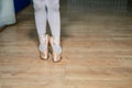 Legs of a little ballerina in a gold ballet shoes and white socks posing tiptoe in ballet hall on the floor. Closeup. Royalty Free Stock Photo