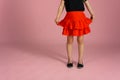 The Legs Of A Little Girl In A Red Skirt And Black Ballet Shoes On A Pink Background. Close-up. The Concept Of Children, Children