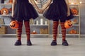 Legs of little girls in Halloween costumes standing holding hands in room with festive decor. Royalty Free Stock Photo