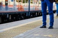 Legs of a man in bright blue trousers and black leather shoes against the background of an arriving train Royalty Free Stock Photo