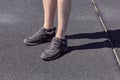 The legs of a man in short shorts and black sneakers. Black and gray asphalt background. Legs of young man in black sneakers.